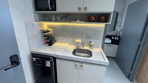 A compact kitchenette with a microwave, coffee machine, sink, and storage cabinets. - Breeze Studio Vista Mar Jardim Oceania (João Pessoa)