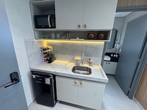 Eine kleine Küchenzeile mit Mikrowelle, Kaffeemaschine, Spüle und Stauraum.
