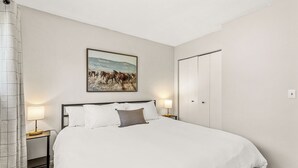 Une chambre d’hôtel avec un grand lit, deux tables de chevet avec des lampes, un tableau représentant des chevaux accroché au mur et une armoire.