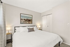Ein Hotelzimmer mit einem großen Bett, zwei Nachttischen mit Lampen, einem Gemälde von Pferden an der Wand und einem Kleiderschrank.