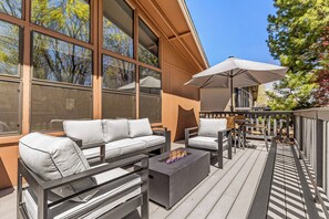 Eine Terrasse mit einer Sitzecke, Sesseln, einer Feuerstelle und einem Sonnenschirm.