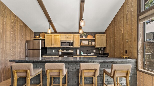 Une cuisine avec des meubles en bois, un plan de travail en granit et des tabourets de bar.