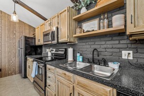 A kitchen with wooden cabinets, a black countertop, stainless steel appliances, and a brick wall. - Cozy 2 BD/1BTH - Family - Country Club - A/C (Flagstaff)