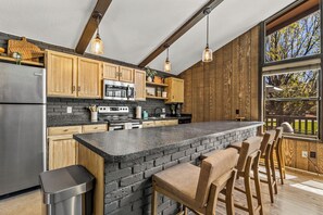 Una cucina moderna con mobili in legno, un frigorifero in acciaio inossidabile, un forno a microonde e una grande isola con sgabelli da bar.