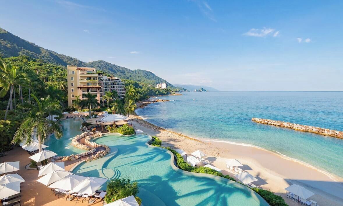 A resort with a swimming pool, beach, and mountain backdrop.