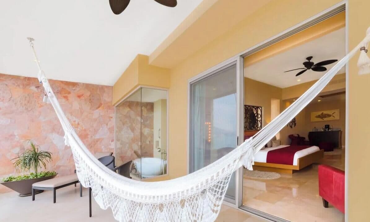 A room with a hammock, a bed, a red sofa, and a glass door leading to another room.