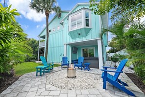 Ein türkisfarbenes Haus mit einer Terrassenanlage, die Sitzgelegenheiten und eine Feuerstelle bietet.