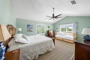 Ein Schlafzimmer mit einem Bett, einem Nachttisch, einer Kommode, einem Deckenventilator und einem Fenster mit Vorhängen.