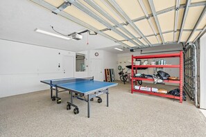 A room with a ping pong table, a red metal shelf unit, and a bicycle. - Sleeps 10 • Hot tub • Games • 5 Mins to Beach (Jupiter)