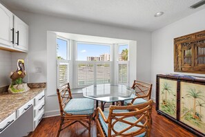A dining area with a round glass table, four wicker chairs, a decorative bird sculpture, and a painting of palm trees. - Sleeps 10 • Hot tub • Games • 5 Mins to Beach (Jupiter)