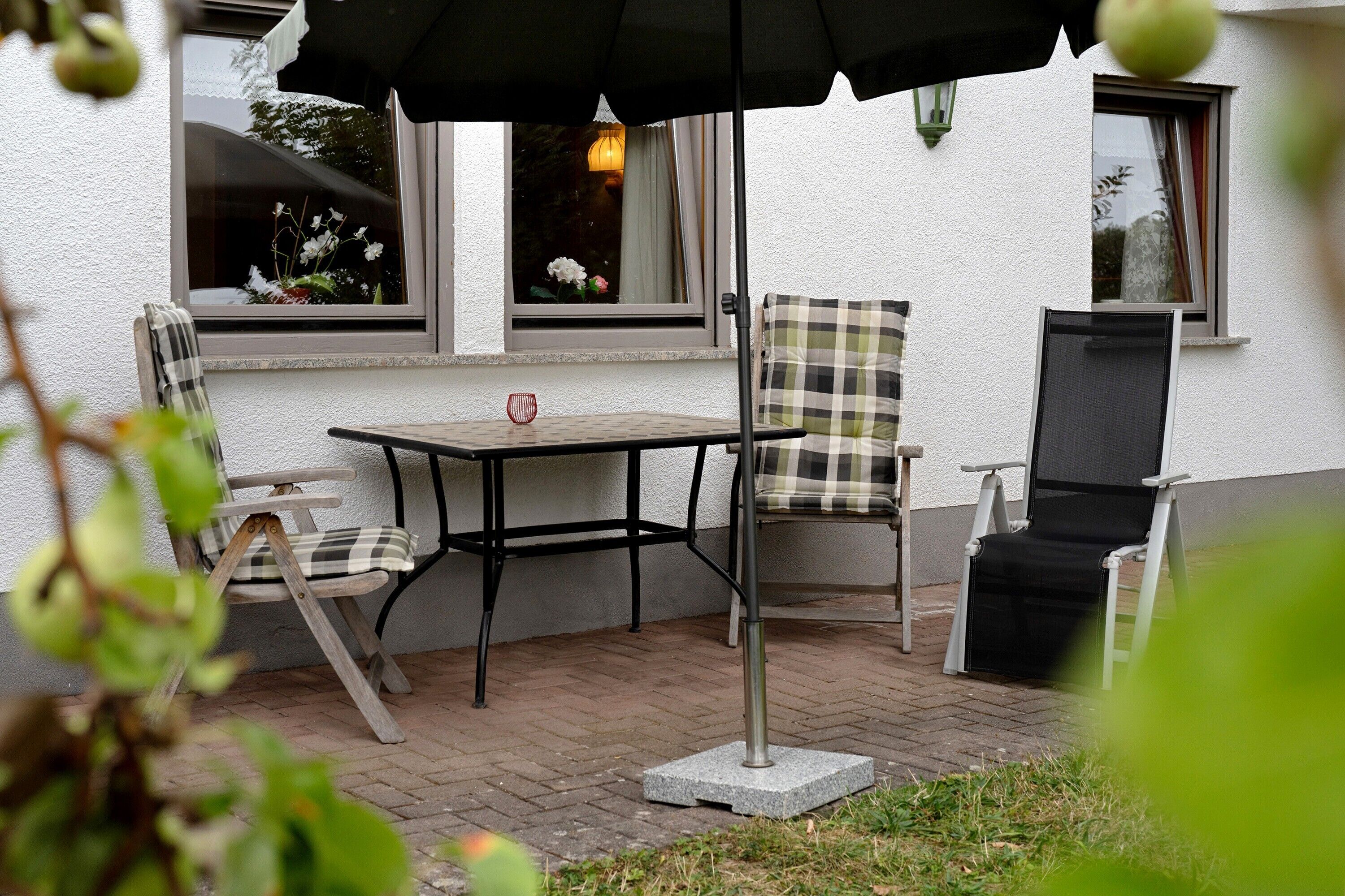 An outdoor patio with a table and chairs, a black umbrella, and a window with a view of the sky.