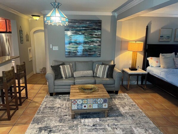 Ein Wohnzimmer mit Sofa, Couchtisch, Lampe und einem Gemälde an der Wand.