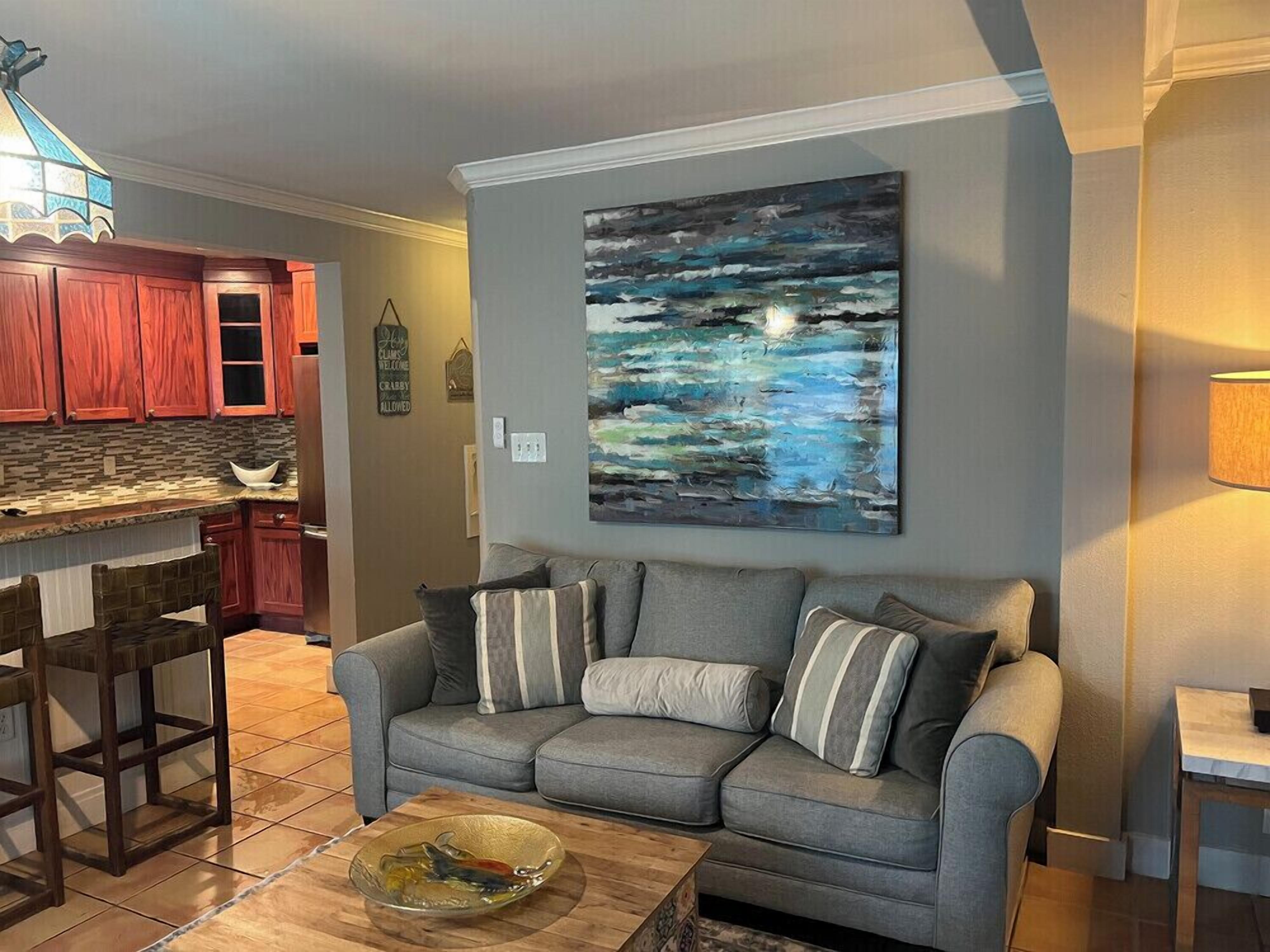 Un salon avec un canapé gris, une table basse en bois et un tableau accroché au mur.