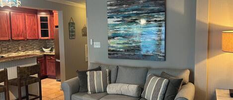 A living room with a grey sofa, a wooden coffee table, and a painting on the wall.