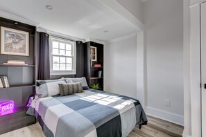 Een slaapkamer met een bed, een raam met gordijnen, een boekenkast en een neonbord.