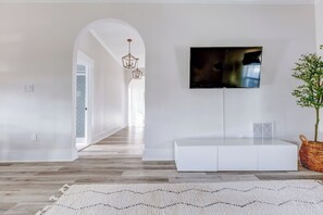 Ein modernes Wohnzimmer mit einer weißen Unterhaltungseinheit, einem flachbildfernseher darüber, einem Holzboden und einem großen weißen Teppich.