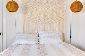 A bed with a patterned bedspread, two pillows, and a macramé wall hanging above. - Historic Concord Mill House with Fenced Backyard (Concord)