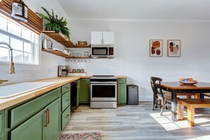 A kitchen with green cabinets, a microwave, a stove, and a dining area with a table and chairs. - Historic Concord Mill House with Fenced Backyard (Concord)