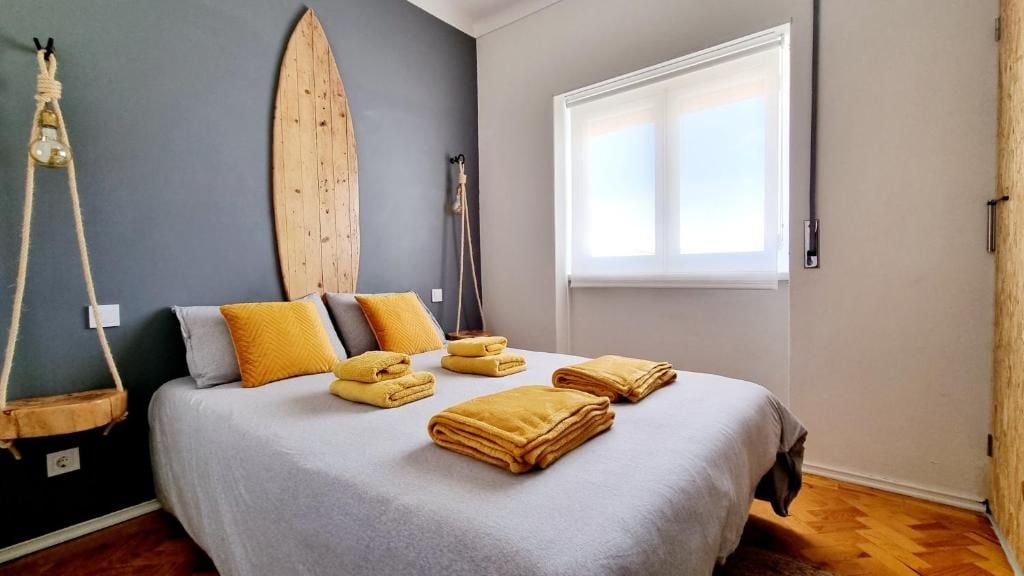 A bedroom with a bed, pillows, a surfboard, a hanging light, and a window.