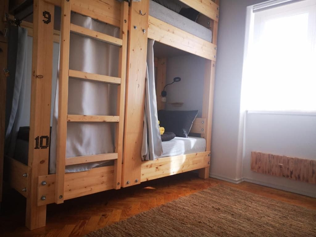 A bunk bed with a wooden frame, a desk with a chair, and a window with curtains.