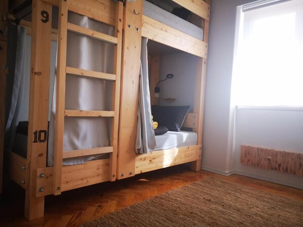 A bunk bed with a wooden frame, a desk with a chair, and a window with curtains.