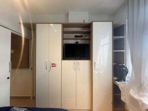 Ein Zimmer mit Kleiderschrank, Fernseher und Ventilator.