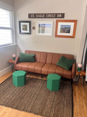 A room with a brown leather sofa, two green ottomans, a woven rug, and three framed pictures on the wall. - Cozy 2-bedroom house with the Columbia View that will take your breath away. (Stevenson)