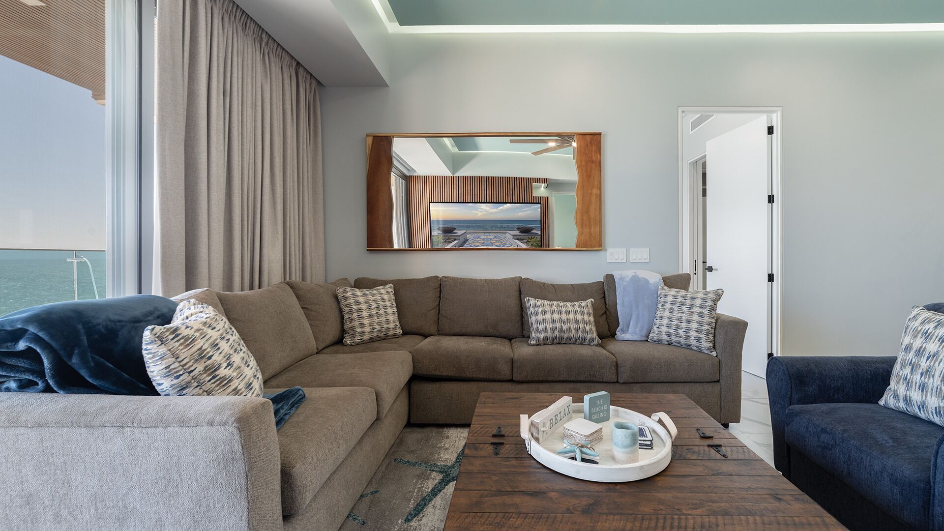 A modern living room with a sectional sofa, a coffee table with a tray, and a large mirror above the sofa.