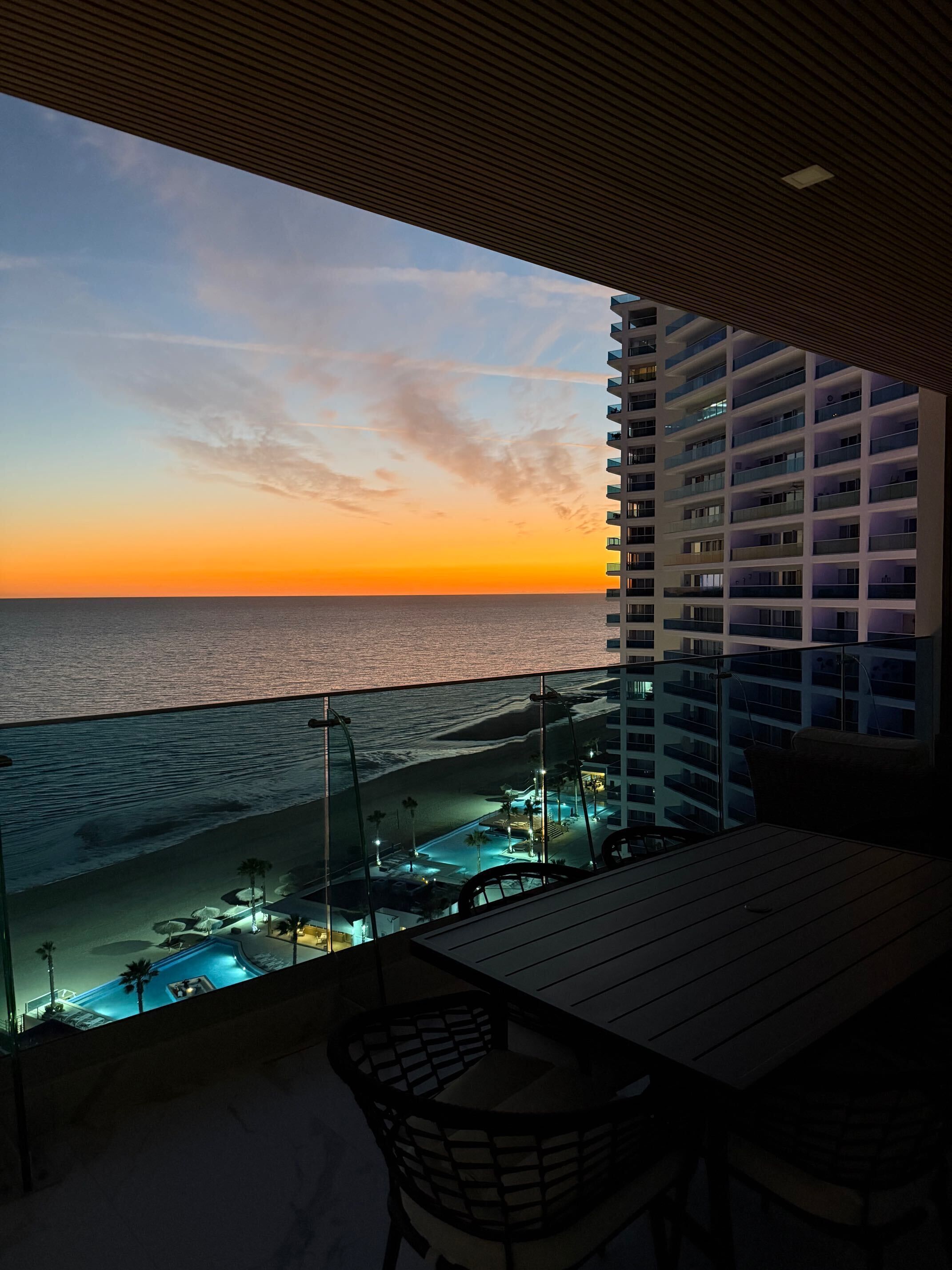 Ein Balkon mit Blick auf den Ozean im Abendlicht, ein Poolbereich und ein Hochhaus im Hintergrund.
