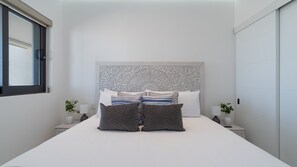 Quarto moderno com uma cama grande, cabeceira decorativa, abajures e uma janela.