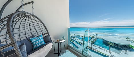 Un balcón con una silla colgante, una mesita y vista a un complejo turístico.