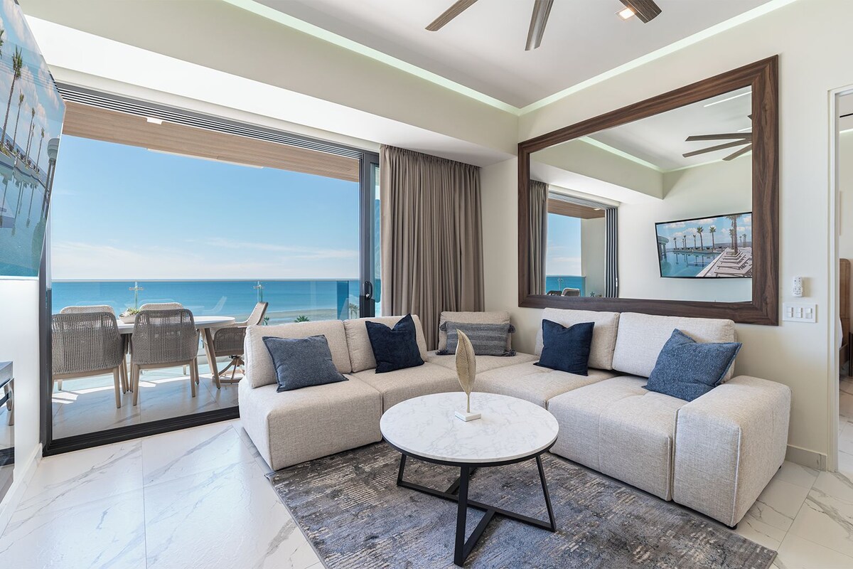 A modern living room with a large window overlooking the ocean, a sectional sofa, a round coffee table, and a view of the sea.