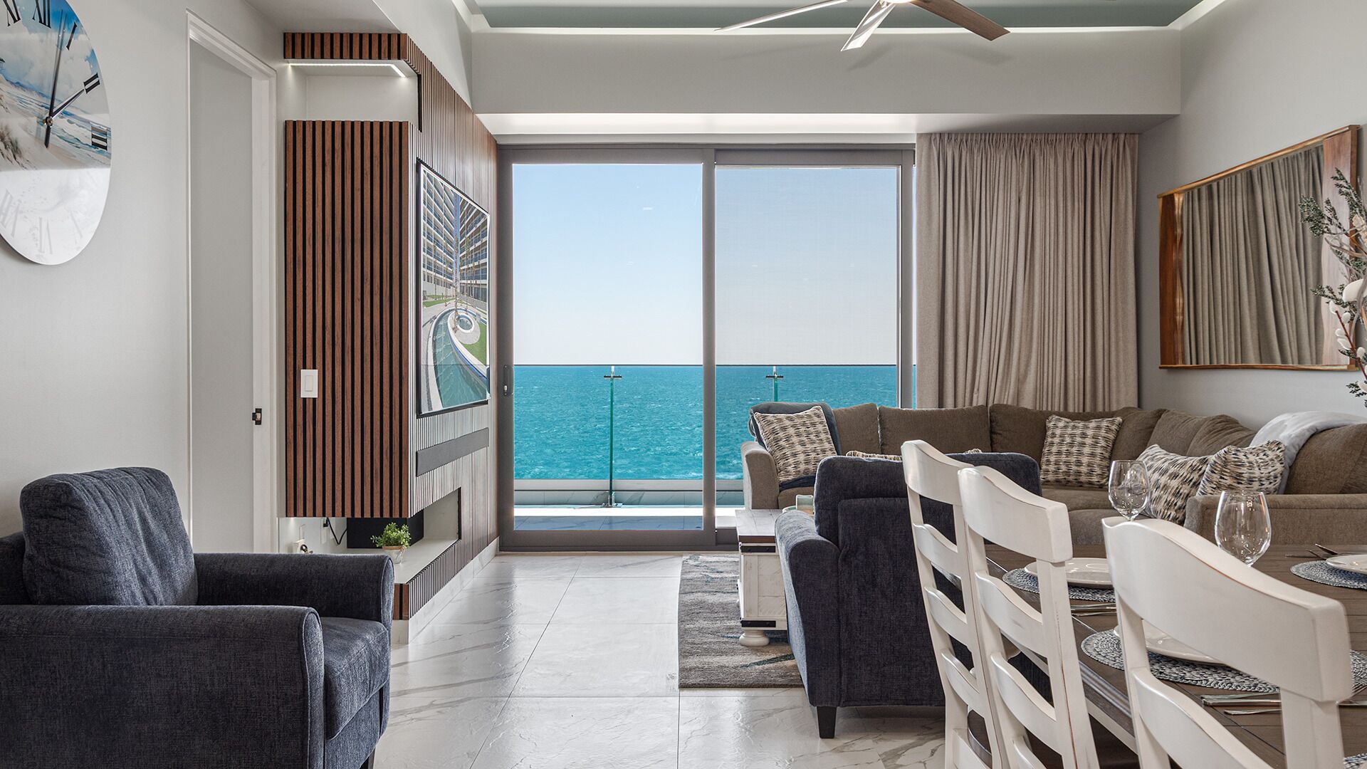 Una sala de estar moderna con vista al mar, un ventilador de techo y un ventanal grande.