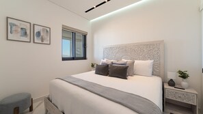 Un dormitorio moderno con una cama grande, una mesita de noche, una ventana y dos obras de arte enmarcadas en la pared.