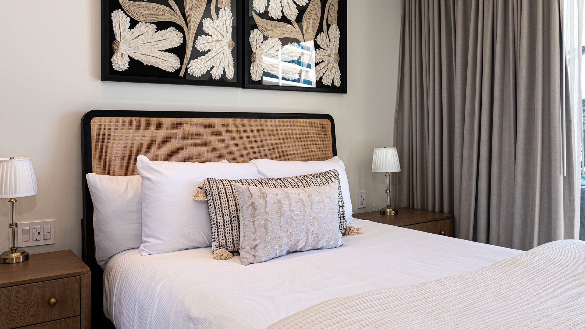 Une chambre d’hôtel avec un lit, deux tables de chevet, une lampe et des œuvres d’art accrochées au mur.