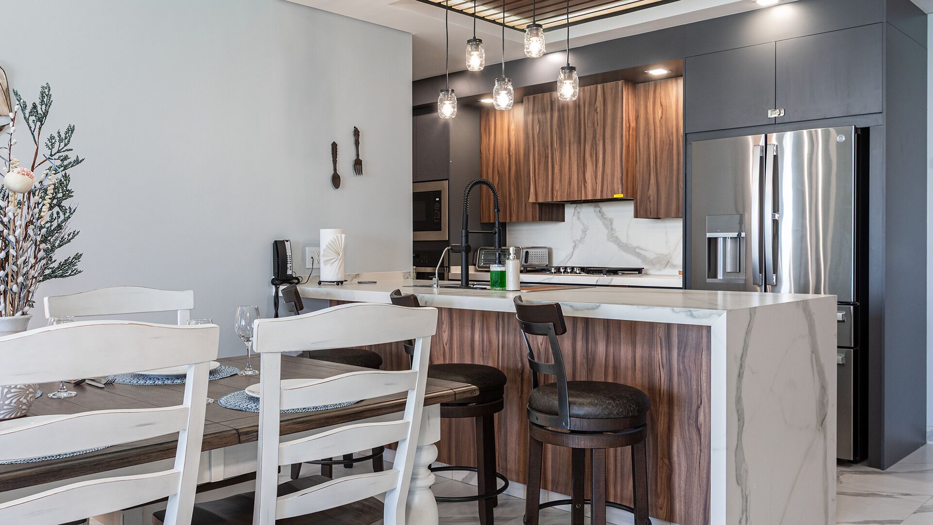 A modern kitchen with a central island, bar stools, and a dining table with chairs.