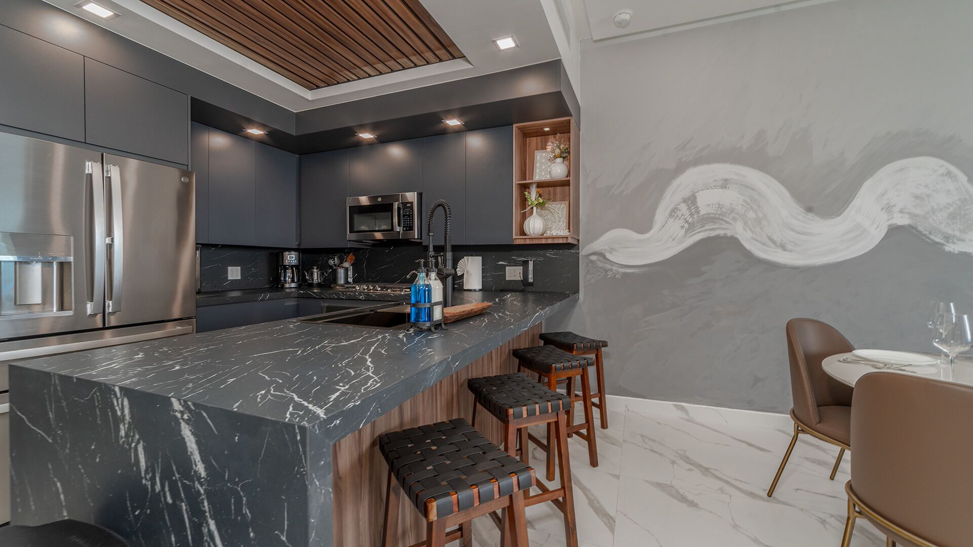Una cocina moderna con armarios oscuros, encimera de mármol y taburetes de bar.