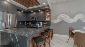 A modern kitchen with dark cabinetry, a marble countertop, and bar stools. - Encantame Soleil (Puerto Peñasco)