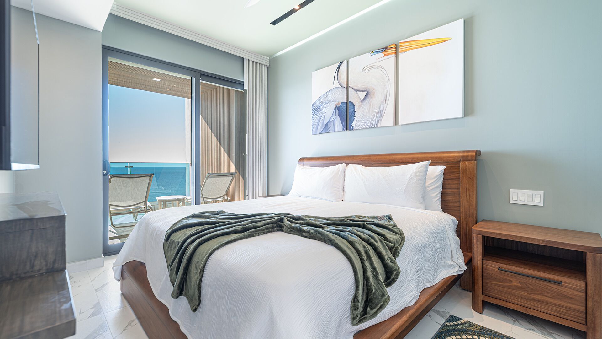 A hotel room with a bed, a nightstand, a chair, and a view of the ocean.
