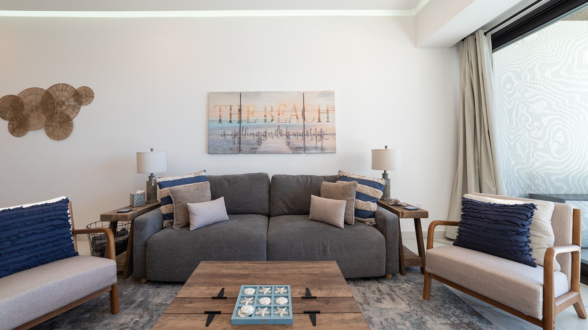 Una sala de estar con un sofá gris, dos sillones, una mesa de centro y una obra de arte colgada en la pared.