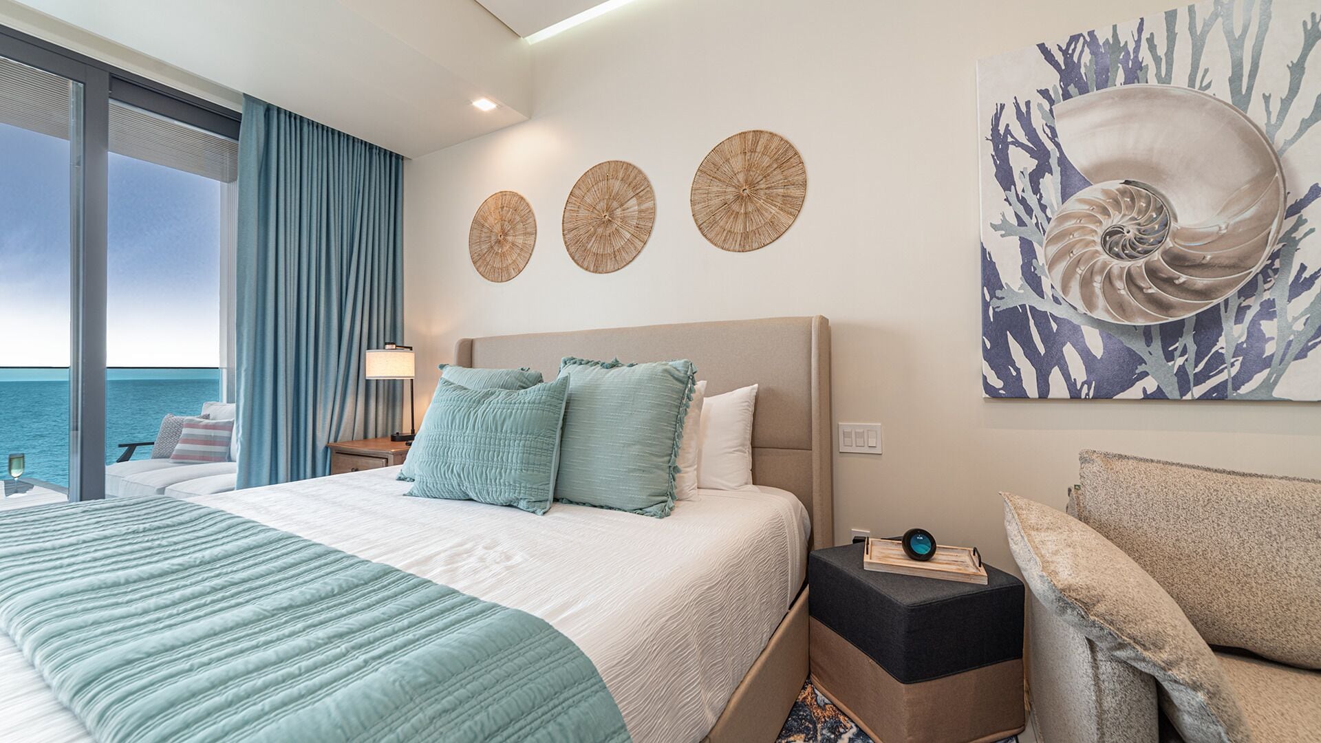 Habitación de hotel con cama, mesita de noche, lámpara y vista al mar.
