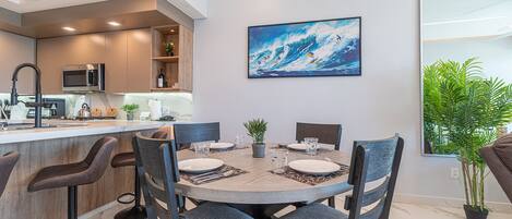 Una cocina moderna con barra, una mesa de comedor para cuatro personas y un cuadro grande de surfistas sobre una ola.