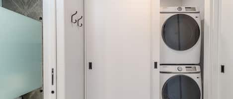 Une buanderie équipée de deux machines à laver Samsung, d’une cabine de douche en verre et d’une porte blanche avec un porte-serviettes.