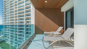 A balcony with two lounge chairs, a wooden slatted wall, and a glass balustrade overlooking a high-rise building. - Encantame Soleil (Puerto Peñasco)
