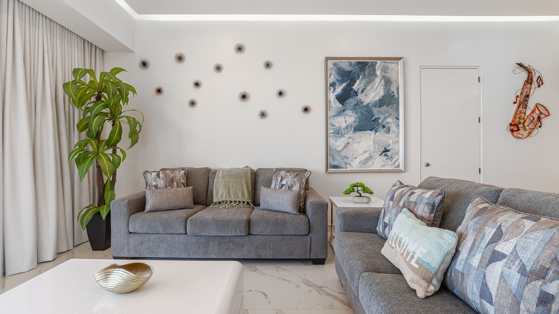 Una sala de estar moderna con un sofá gris, una mesa de centro, una planta en maceta y un cuadro abstracto grande en la pared.