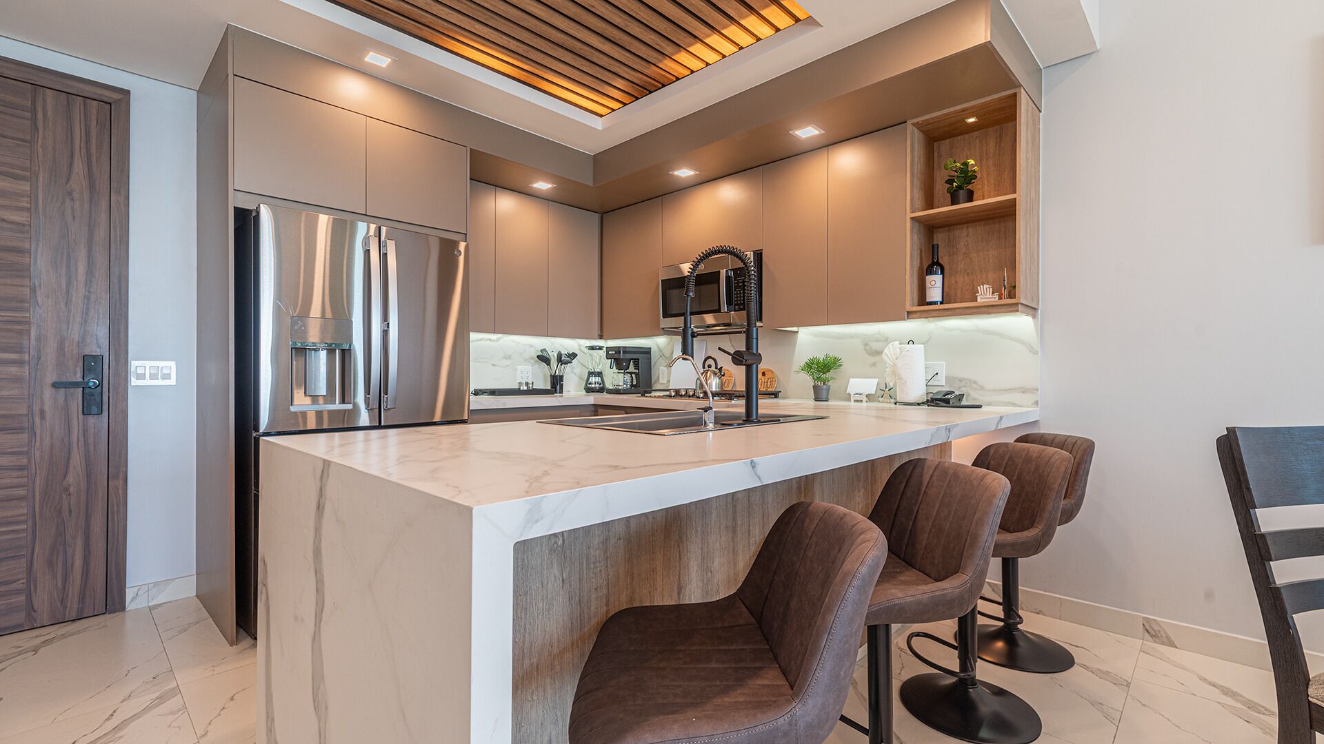 Une cuisine moderne dotée d’un îlot central, de tabourets de bar et d’appareils électroménagers intégrés.