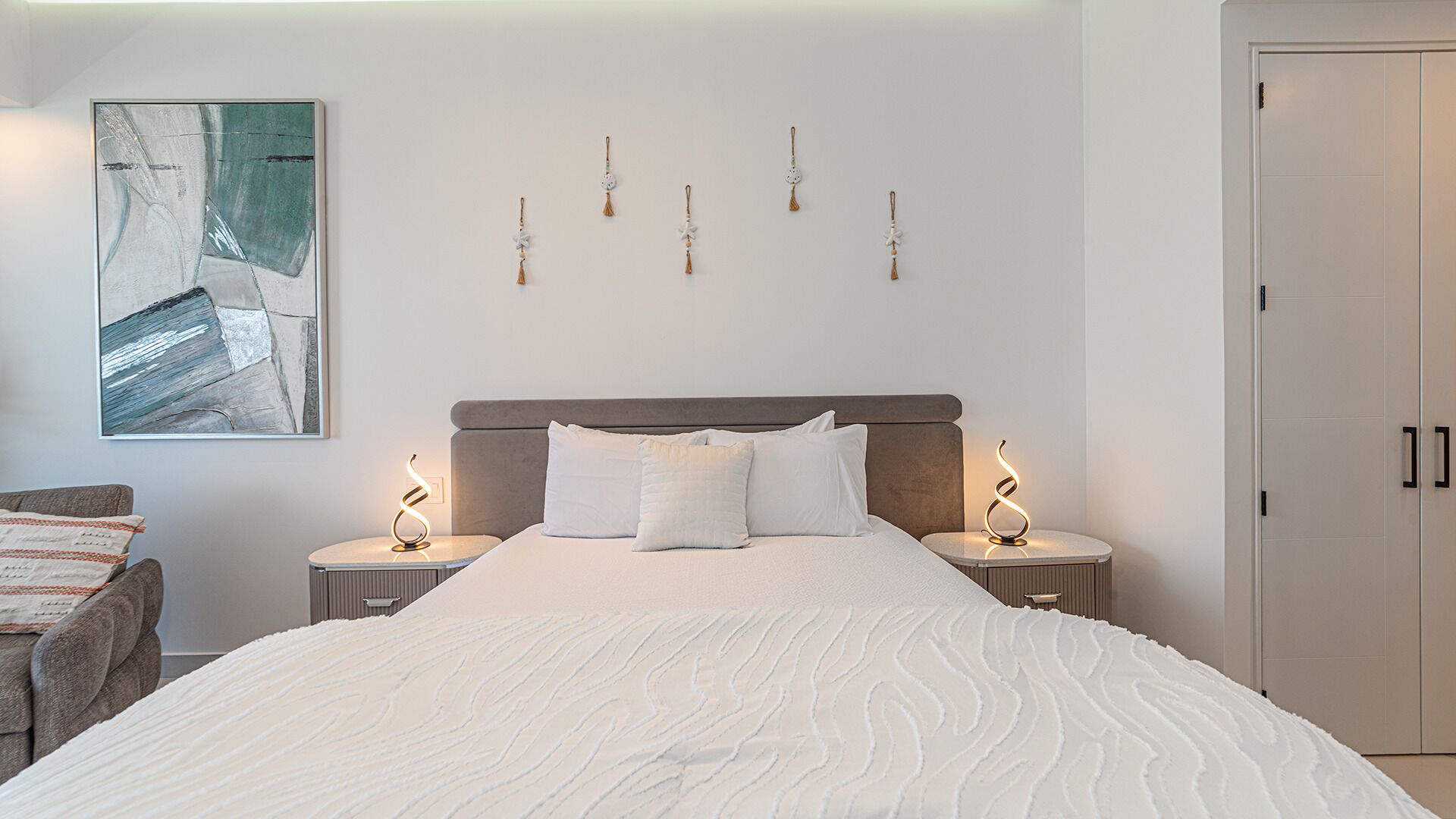 Une chambre à coucher avec un grand lit, deux tables de chevet, une œuvre d’art accrochée au mur et une porte.