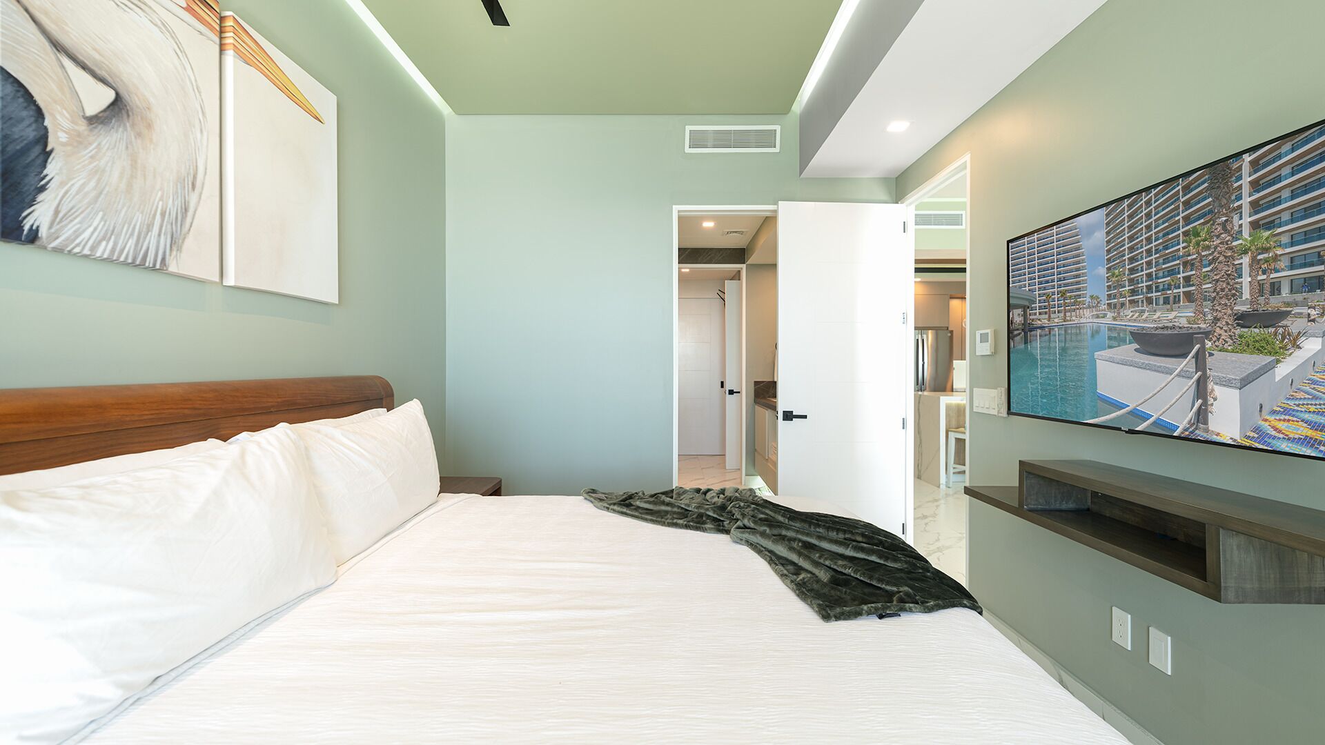 A hotel room with a bed, a TV mounted on the wall, and a painting of a swan.