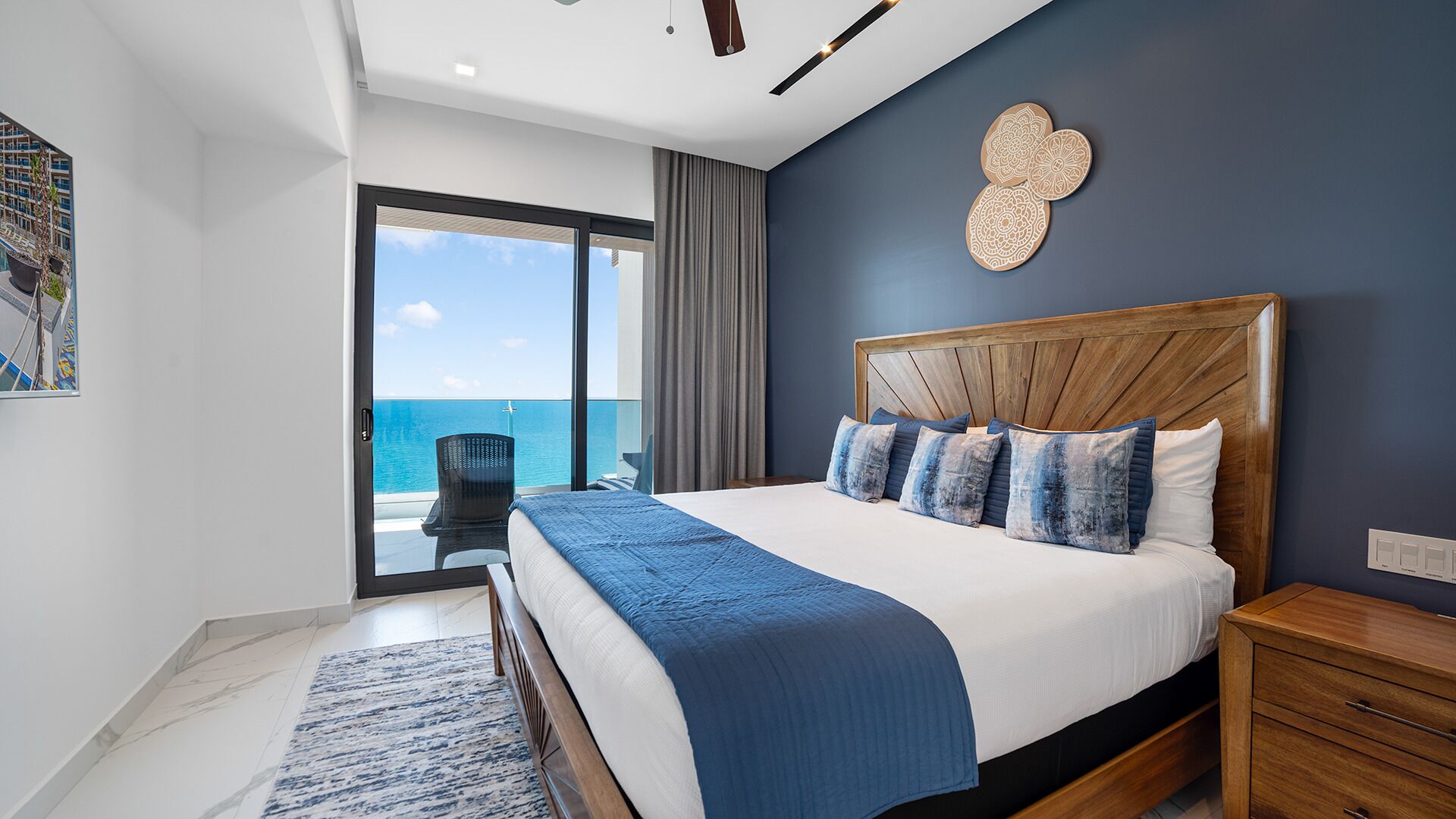 A bedroom with a large bed, a view of the sea, and a balcony with a chair.