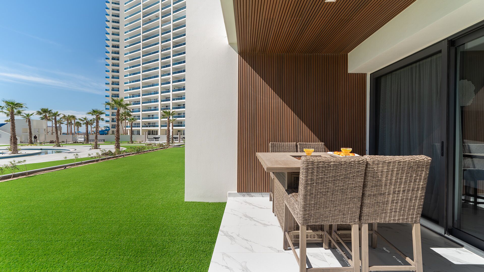A modern outdoor seating area with a pool view, a tall building in the background, and a clear sky.